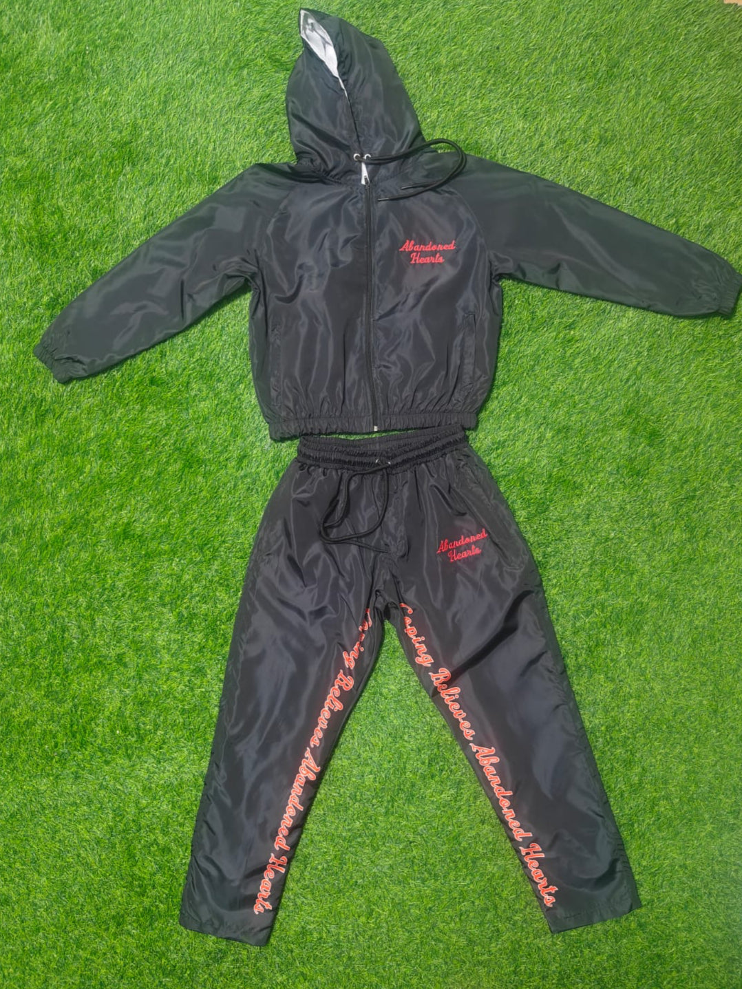 Black windbreaker and pants set with red text on a green grass background